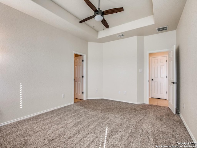 spare room featuring a tray ceiling, a ceiling fan, visible vents, and light colored carpet