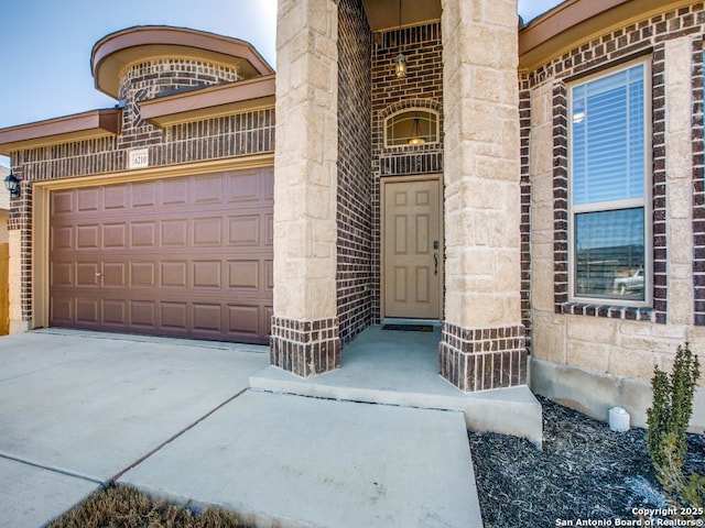 entrance to property with driveway, stone siding, an attached garage, and brick siding