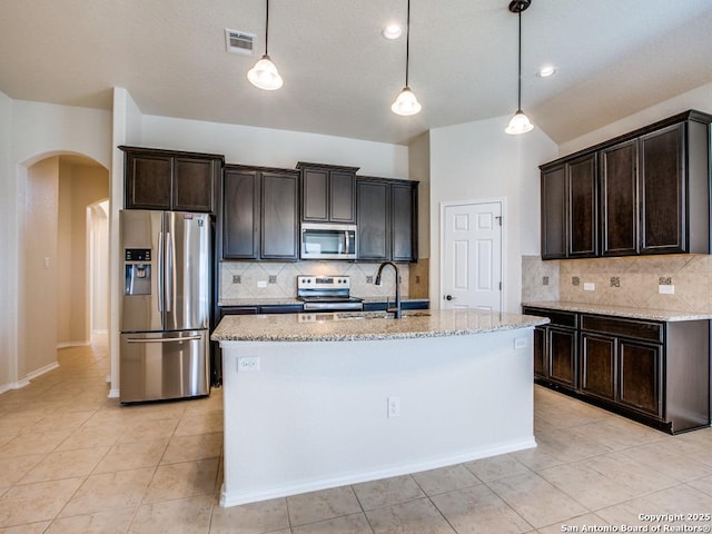 kitchen with stainless steel appliances, arched walkways, dark brown cabinetry, and light stone countertops