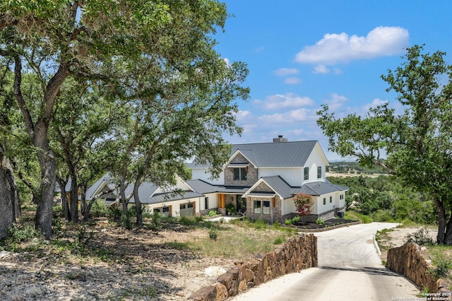 modern inspired farmhouse featuring a chimney, concrete driveway, a standing seam roof, metal roof, and stone siding