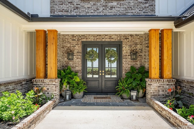 view of exterior entry featuring board and batten siding, french doors, and brick siding