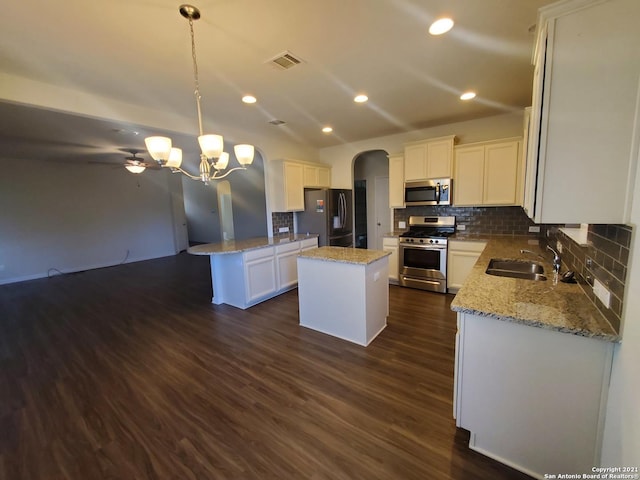 kitchen featuring arched walkways, stainless steel appliances, dark wood-style flooring, a kitchen island, and a sink