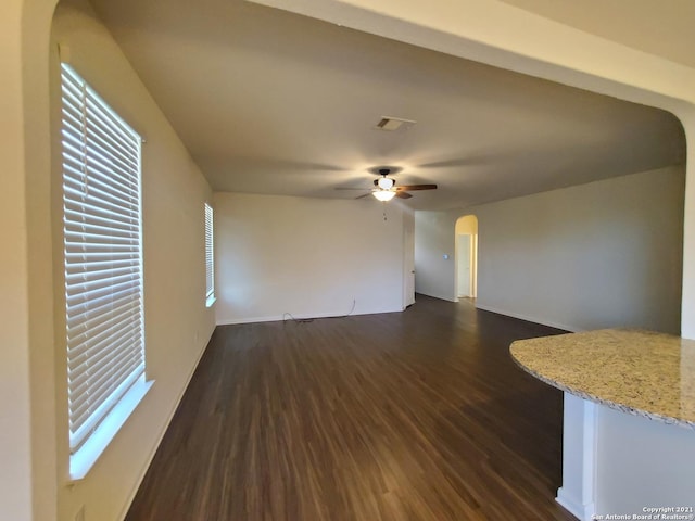 unfurnished living room with arched walkways, dark wood-style flooring, visible vents, a ceiling fan, and baseboards