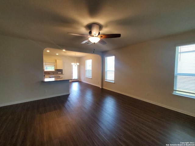 unfurnished living room featuring dark wood-type flooring, visible vents, baseboards, and ceiling fan with notable chandelier