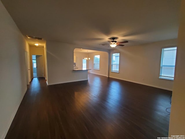 unfurnished living room with dark wood-style floors, baseboards, visible vents, and ceiling fan with notable chandelier