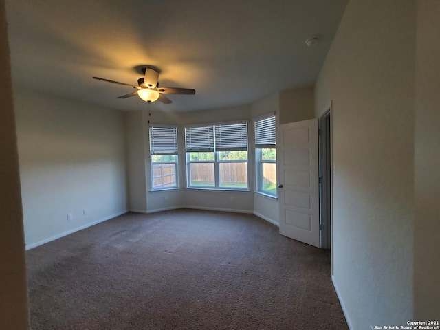 empty room with dark colored carpet, ceiling fan, and baseboards