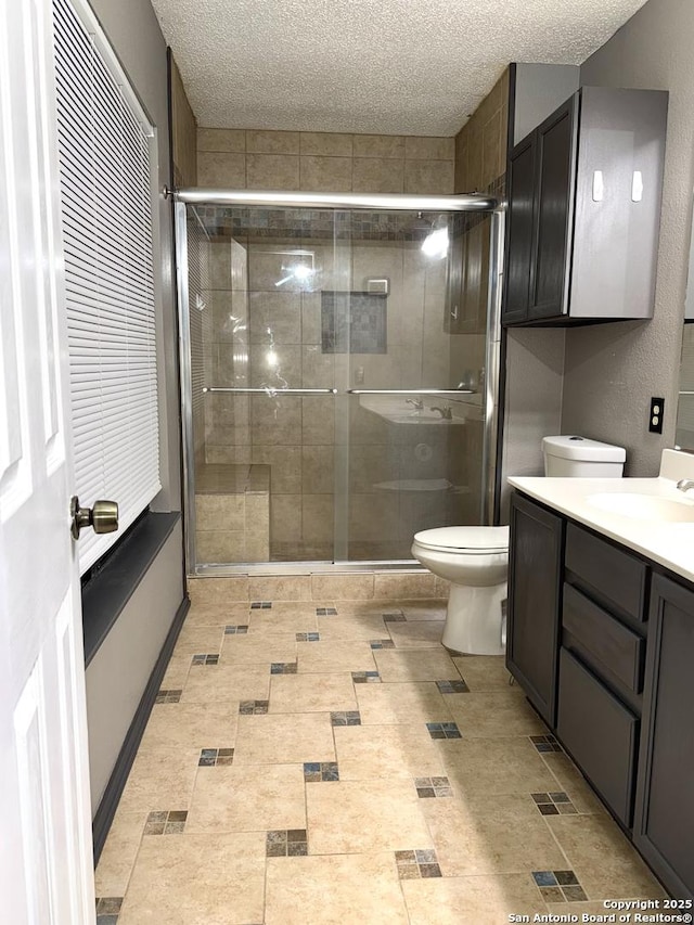 full bathroom featuring a textured ceiling, a stall shower, vanity, and toilet