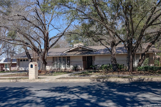 ranch-style home with metal roof, a garage, covered porch, brick siding, and a standing seam roof