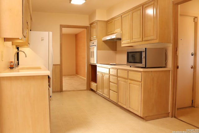 kitchen featuring under cabinet range hood, a sink, white oven, light floors, and stainless steel microwave