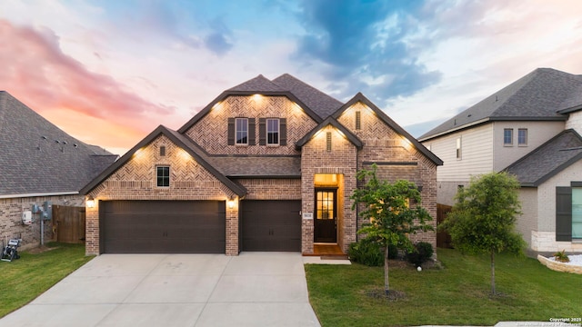 french country inspired facade with concrete driveway, brick siding, a front lawn, and a shingled roof