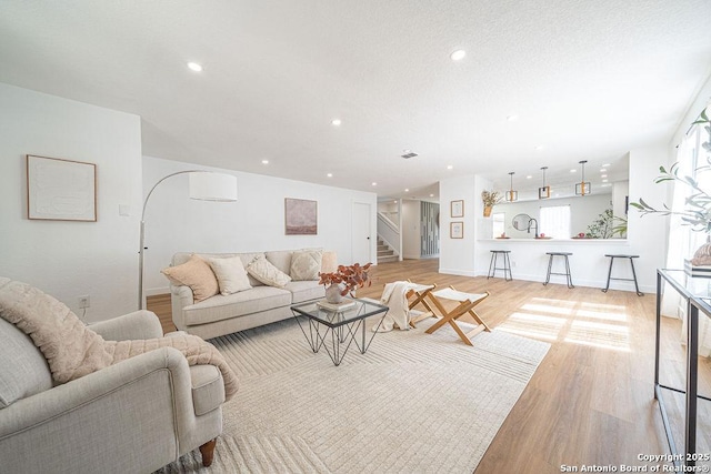 living room with baseboards, light wood-style flooring, stairway, a textured ceiling, and recessed lighting