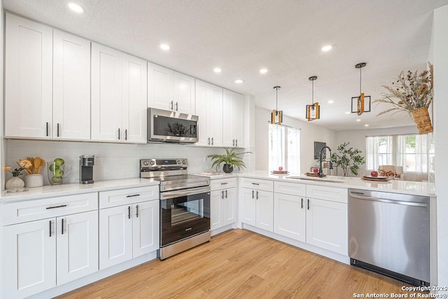 kitchen with light wood-style flooring, a sink, white cabinets, light countertops, and appliances with stainless steel finishes