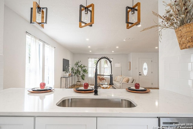 kitchen featuring light stone counters, open floor plan, a textured ceiling, white cabinetry, and a sink