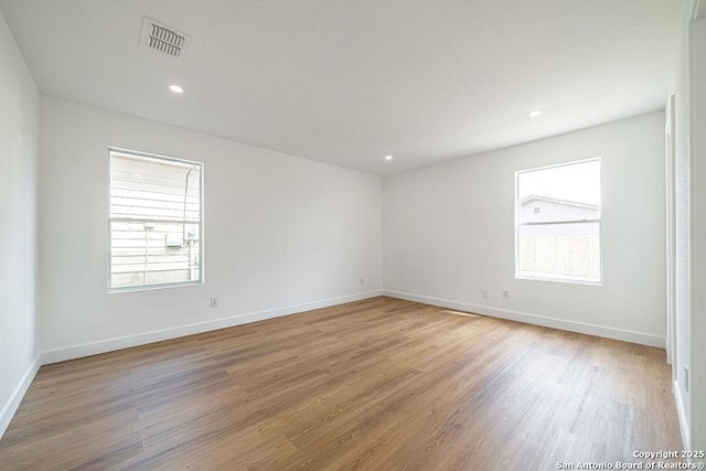 empty room with light wood finished floors, a wealth of natural light, visible vents, and baseboards