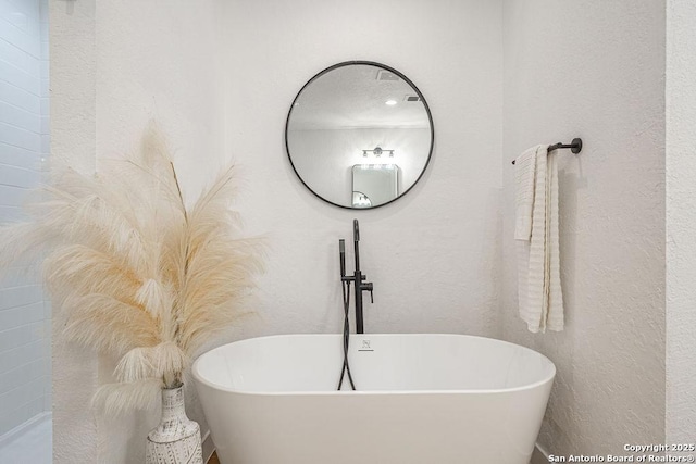 bathroom featuring a soaking tub, a sink, and a textured wall