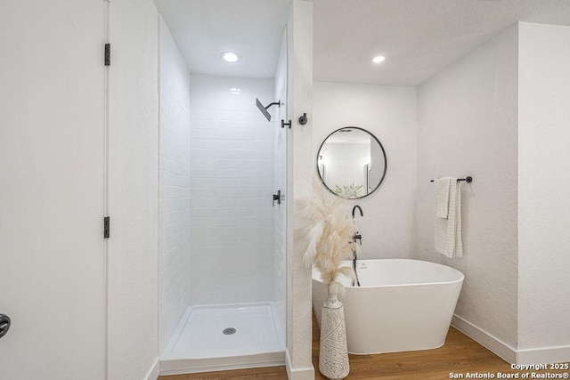 full bathroom featuring baseboards, wood finished floors, a freestanding bath, a shower stall, and recessed lighting