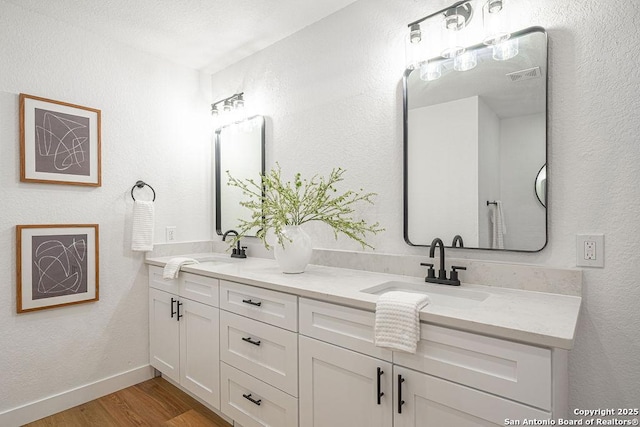 full bathroom with double vanity, a sink, baseboards, and wood finished floors