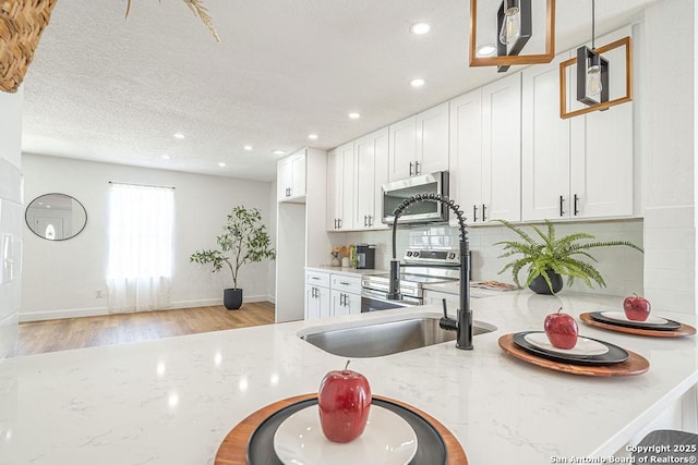 kitchen featuring appliances with stainless steel finishes, white cabinetry, light wood-style flooring, and light stone counters