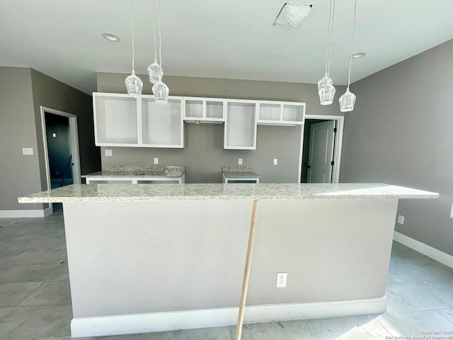 kitchen with baseboards, hanging light fixtures, a kitchen island, and white cabinets