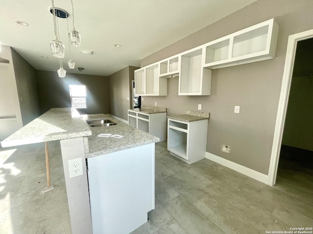 kitchen with a center island with sink, baseboards, light stone counters, white cabinetry, and a sink