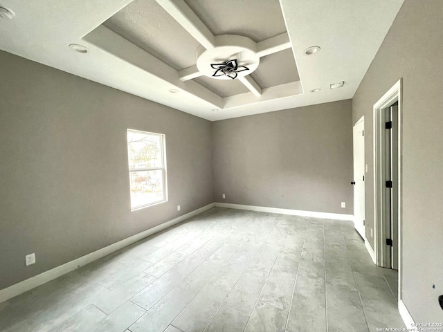 empty room featuring wood finished floors, a raised ceiling, a ceiling fan, and baseboards