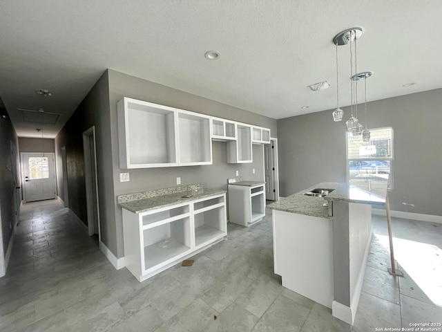 kitchen with decorative light fixtures, white cabinets, an island with sink, light stone countertops, and baseboards