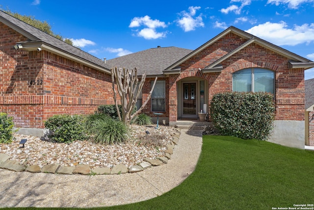 ranch-style house with roof with shingles, a front yard, and brick siding