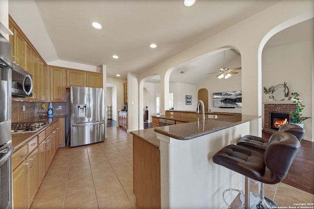 kitchen featuring tasteful backsplash, dark stone counters, a breakfast bar area, stainless steel appliances, and light tile patterned flooring