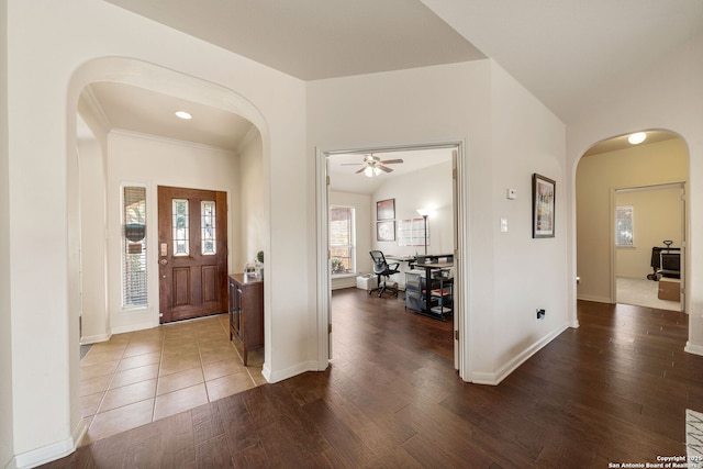 foyer featuring arched walkways, dark wood-style floors, and baseboards