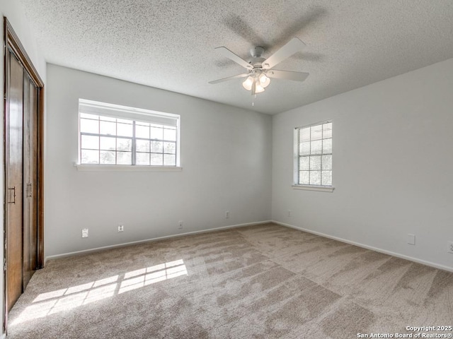 empty room featuring a textured ceiling, carpet floors, a ceiling fan, and baseboards