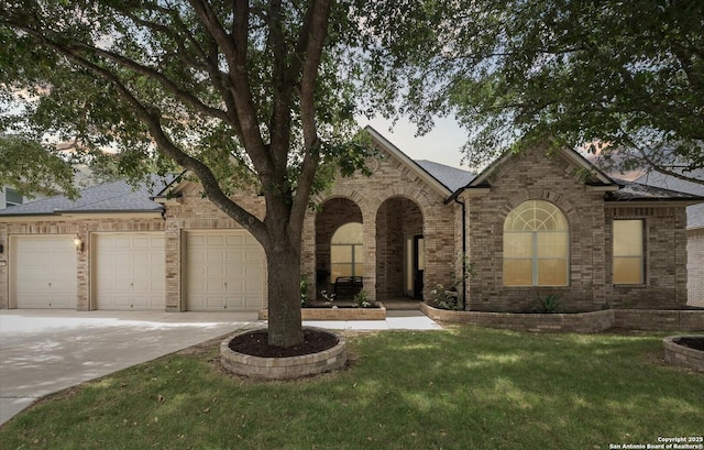 view of front facade with brick siding, roof with shingles, a front yard, a garage, and driveway