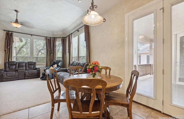 dining space featuring a healthy amount of sunlight, light tile patterned floors, a textured wall, and light colored carpet