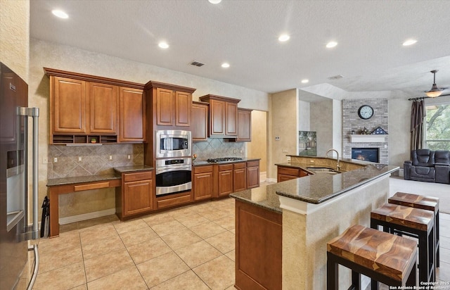 kitchen with brown cabinets, a fireplace, visible vents, appliances with stainless steel finishes, and a sink