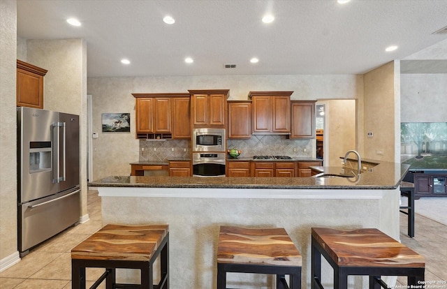 kitchen featuring visible vents, appliances with stainless steel finishes, brown cabinetry, a sink, and a kitchen breakfast bar