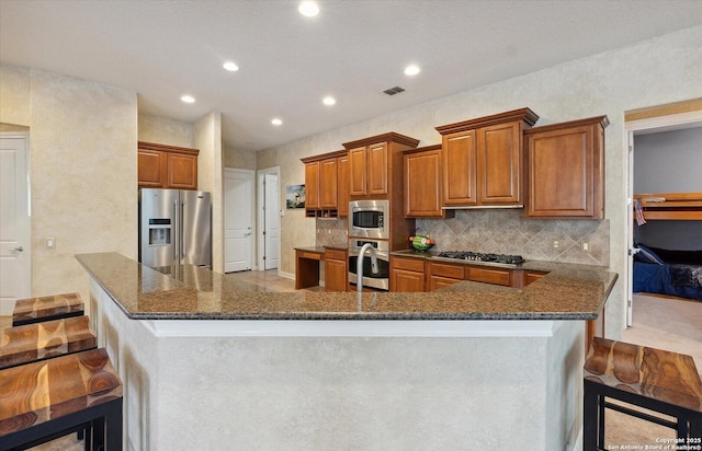 kitchen with visible vents, appliances with stainless steel finishes, brown cabinetry, and dark stone countertops