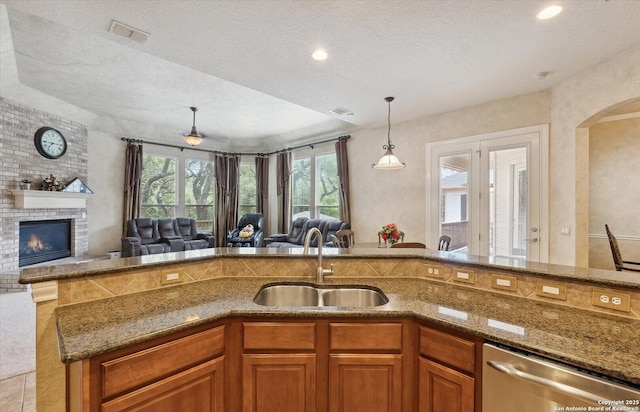 kitchen with stone countertops, a sink, open floor plan, brown cabinets, and dishwasher