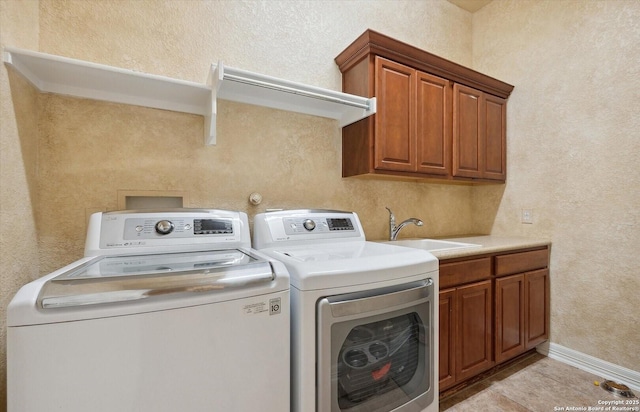 clothes washing area featuring cabinet space, light tile patterned floors, a textured wall, washing machine and clothes dryer, and a sink