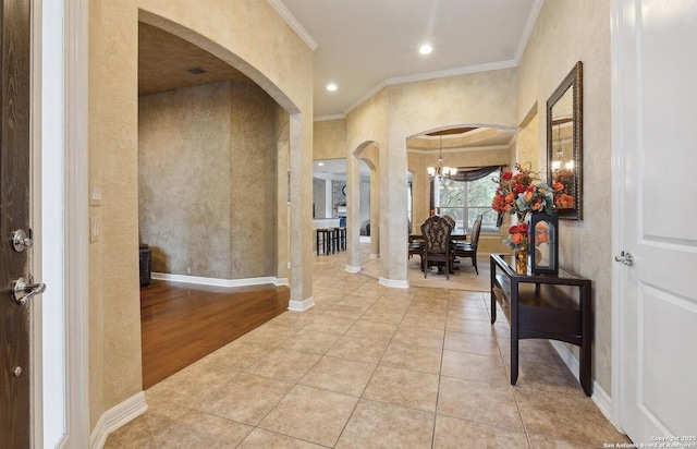 foyer with arched walkways, ornamental molding, a chandelier, tile patterned flooring, and baseboards