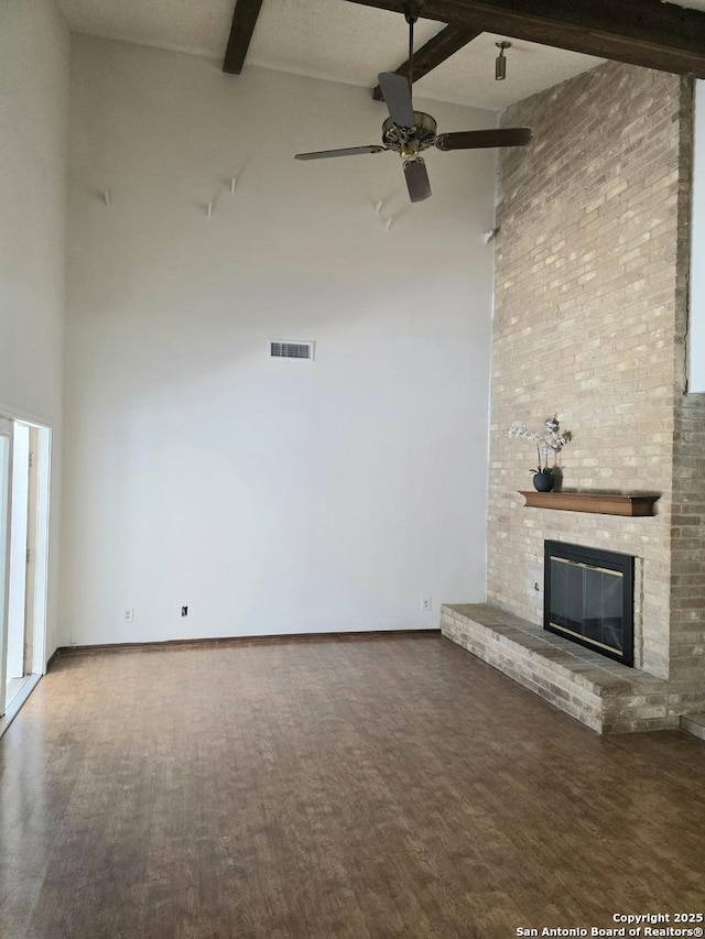 unfurnished living room with beamed ceiling, a brick fireplace, a towering ceiling, and visible vents