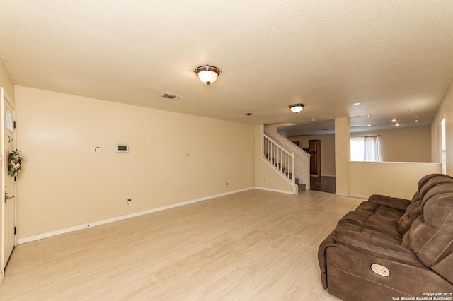 living area featuring light wood finished floors, visible vents, a textured ceiling, baseboards, and stairs