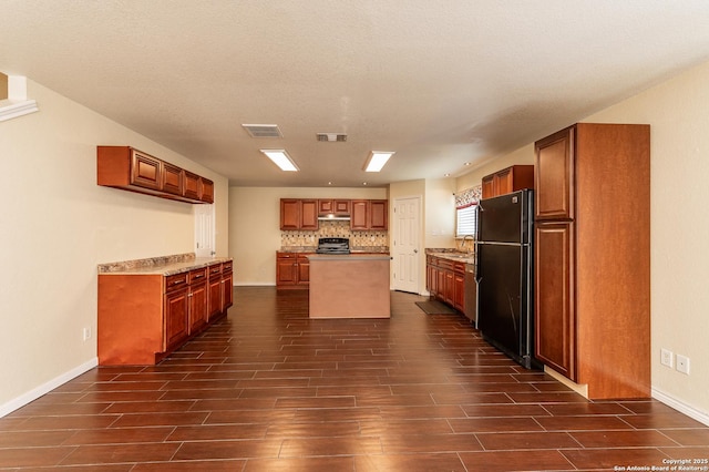 kitchen with under cabinet range hood, wood finish floors, stove, a kitchen island, and freestanding refrigerator