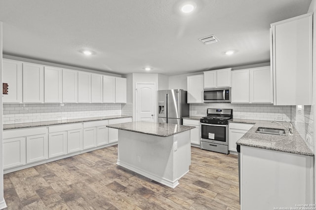 kitchen with light stone counters, a sink, visible vents, appliances with stainless steel finishes, and light wood-type flooring