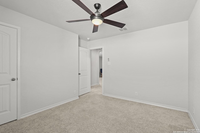 unfurnished bedroom featuring a textured ceiling, light colored carpet, a ceiling fan, baseboards, and visible vents