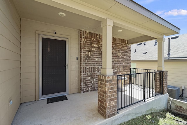 doorway to property with covered porch, brick siding, and central AC unit