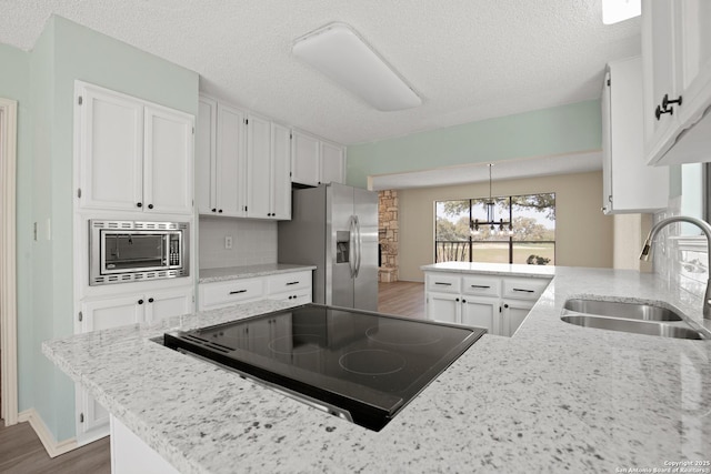 kitchen with tasteful backsplash, appliances with stainless steel finishes, white cabinetry, a sink, and a peninsula