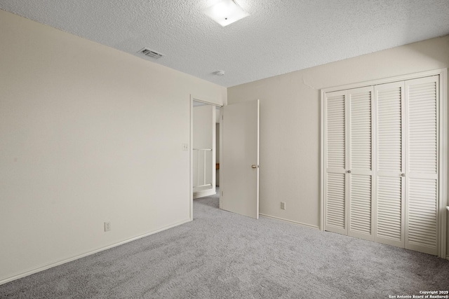 unfurnished bedroom featuring a textured ceiling, carpet floors, visible vents, baseboards, and a closet