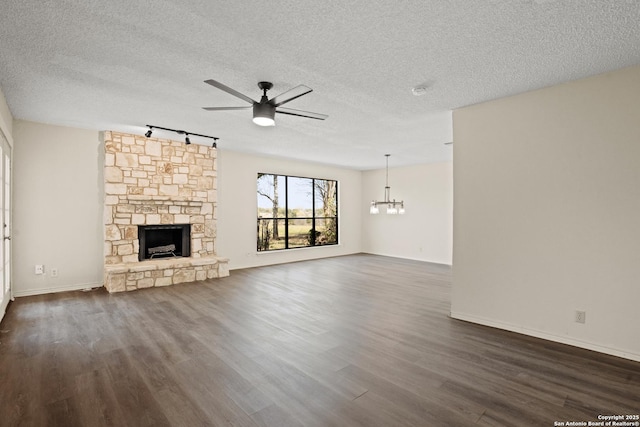 unfurnished living room featuring dark wood-type flooring, a stone fireplace, a textured ceiling, and ceiling fan with notable chandelier