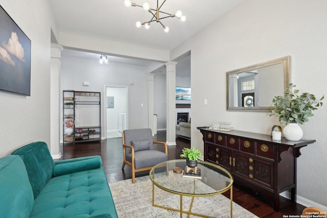 living area with a fireplace, decorative columns, an inviting chandelier, wood finished floors, and baseboards