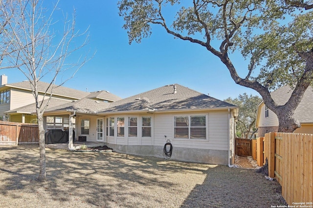 back of property with a shingled roof, a fenced backyard, and a patio