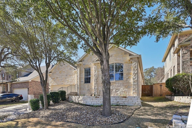 view of front facade with stone siding, an attached garage, fence, and driveway